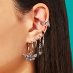 Close-up of an ear with multiple silver earrings and a cuff against a teal background - Takes you to Clarice Charm
